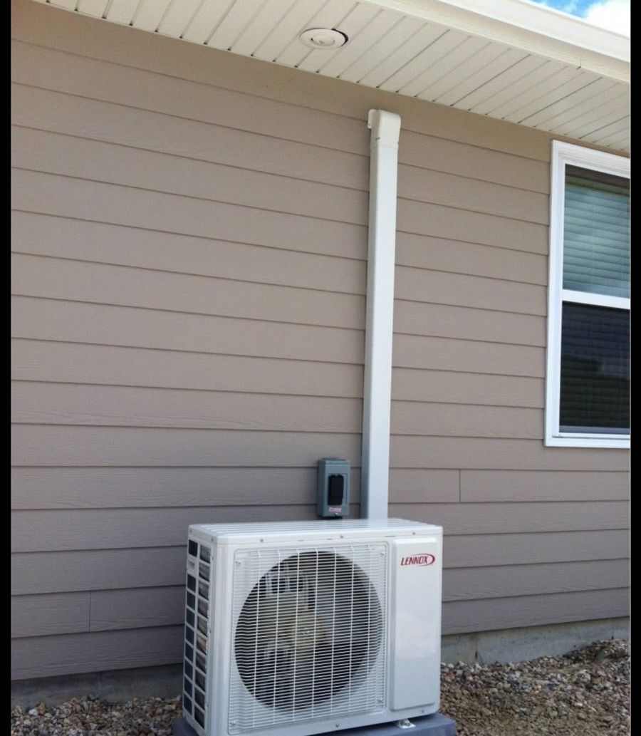 A mini split outdoor unit mounted on a pad beside a house